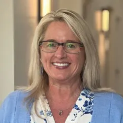 Blonde staff wearing glasses and a blue cardigan over a white floral blouse