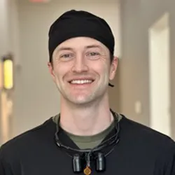 Dentist wearing hair cap and black scrubs smiling