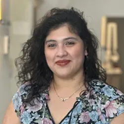 Dark curly haired staff wearing a blue and purple floral short sleeved blouse