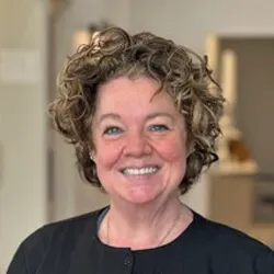 Curly haired female staff in a black cardigan smiling